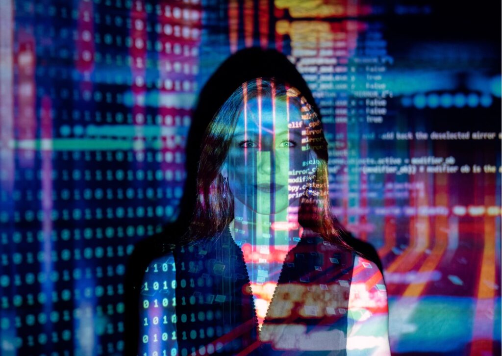 A woman is standing in front of a wall. A projection of code is covering both her and the wall